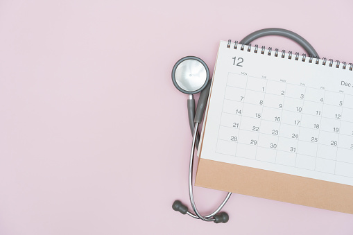 Top view of stethoscope and calendar on the pink table background flat lay, schedule to check up healthy concept