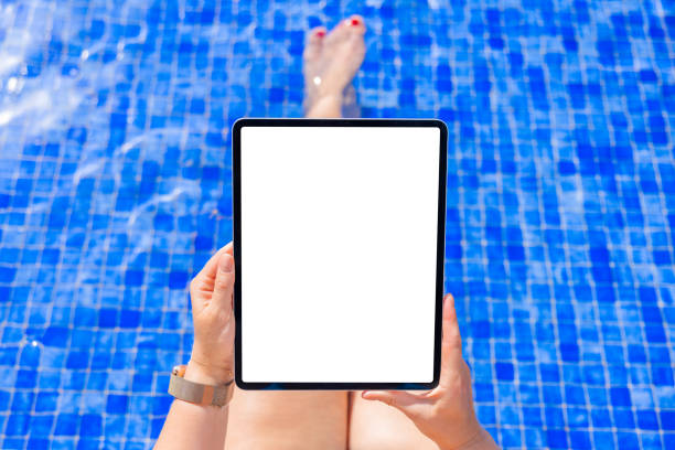 istock Woman by the pool holding tablet computer with empty white screen 1418649218