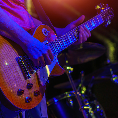 The guitarist plays the guitar in the spotlight. Hands of a Guitar player playing the guitar. Selective focus. Soft focus