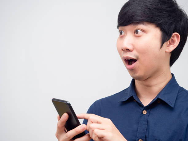 istock Asian man cheerful feeling happy holding mobile phone looking at space white background 1418655474