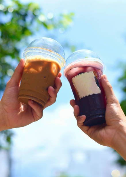 istock Hand clinking plastic cups of coffee and mulberry tea closeup 1418659366
