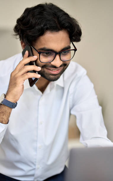 istock Smiling indian bank manager talking on phone consulting client using pc. 1418691351