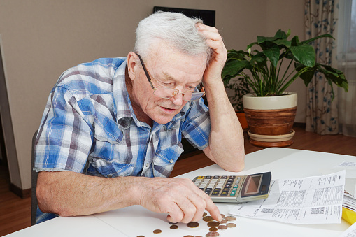 Upset depressed Senior man sitting at the table and calculating finances. Old man checking bills. Man counting coins on the table. Pension calculation concept