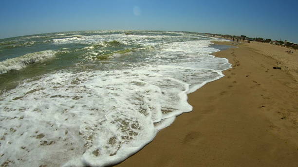 istock Sea wave with white foam rolls over sandy shore of beach. Top view. 1418694829