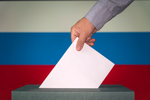 russia the symbol of elections. Male hand puts down a white sheet of paper with a mark as a symbol of a ballot paper against the background of the russia flag