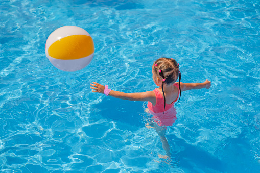 A girl in a pink swimsuit runs after an inflatable ball in the swimming pool. Water games at the aquapark