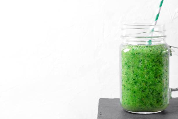 istock Background with green smoothie in glass jar with straw on white 1418718322
