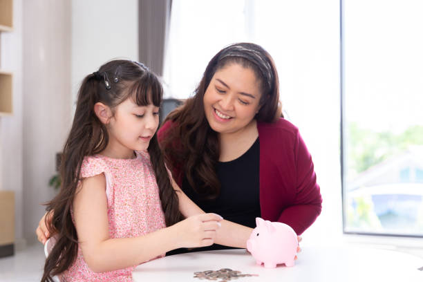 smiling happy daughter child collect coin for money saving for education and economic growth with mother in piggy bank stock photo