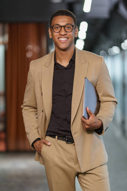 istock Handsome smiling african businessman with documents standing in modern coworking 1418726520