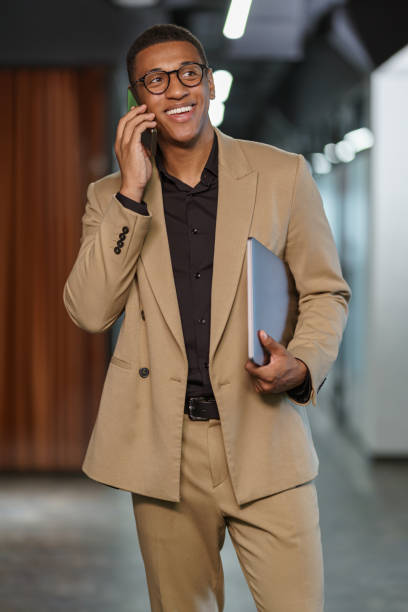 istock Handsome smiling african businessman talking phone while standing in modern coworking 1418726558