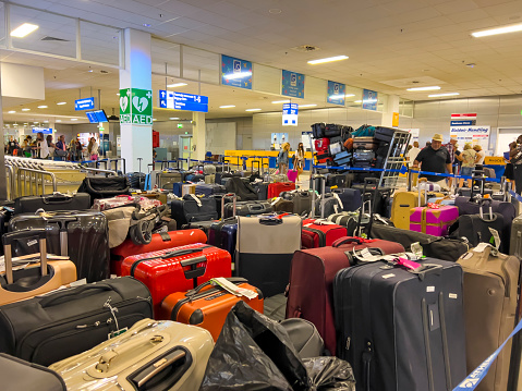 Athens, Greece - July 26, 2022:  Lines of luggage mess at Athens International Airport Eleftherios Venizelos during summer vacation. Baggage chaos at Eurpoean airports. Many suitcases waiting inside terminal as result of ground personnel staff shortage. Travel theme background, copy space.