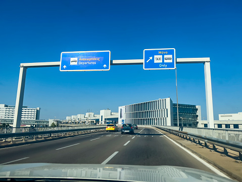 Athens, Greece - July 31, 2022: Cars driving into the departure area at Athens International Airport Eleftherios Venizelos. High up way signs directing the way forward. Travel theme background on sunny day