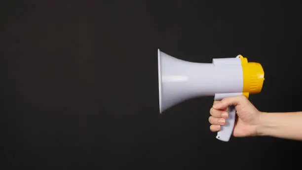 Photo of Hand is holding yellow megaphone on black background.