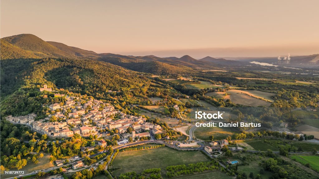 Panoramic drone view of one of the most beautiful French towns in southern France - Mirmande. Old historic town. Sunset over the surrounding mountains. Chimneys from the power plant in the distance Montelimar Stock Photo