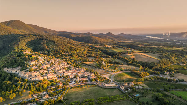 Panoramic drone view of one of the most beautiful French towns in southern France - Mirmande. Old historic town. Sunset over the surrounding mountains. Chimneys from the power plant in the distance Panoramic drone view of one of the most beautiful French towns in southern France - Mirmande. Old historic town. Sunset over the surrounding mountains. Chimneys from the power plant in the distance drome stock pictures, royalty-free photos & images