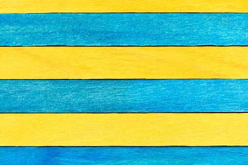 Blue and yellow painted wooden boards. Bright wooden textured background. A wall of alternating blue and yellow wooden planks arranged horizontally.