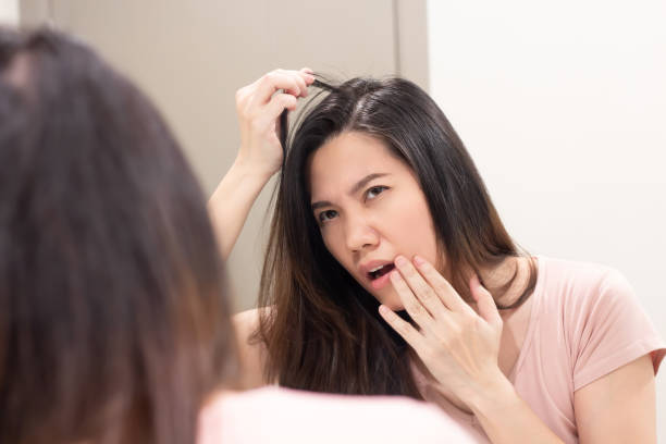 istock Asian beautiful woman look herself through mirror and pull her hair and touch her lip with worry about hair loss and grey hair. 1418757664