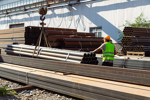 Worker transporting stack of metal pipes with gantry crane in the steel factory