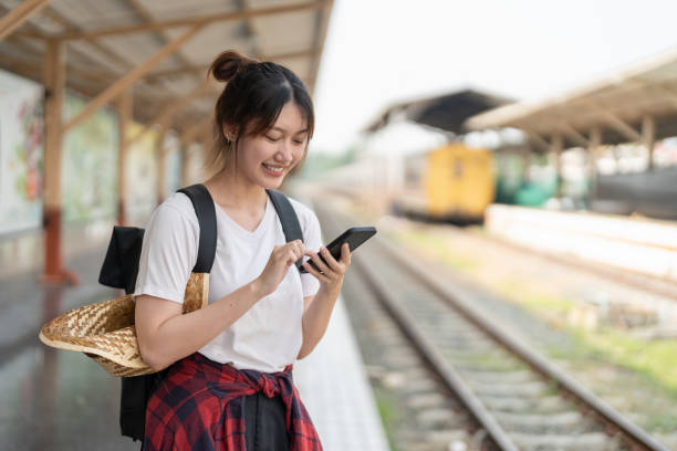 istock Beautiful young asian woman with a backpack using mobile phone while standing near the railroad train on the platform. Cheap travel summer concept 1418763255