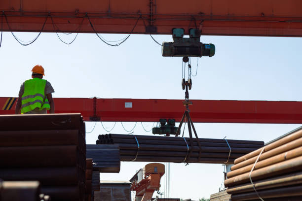 istock Worker transporting stack of metal pipes with gantry crane 1418764134