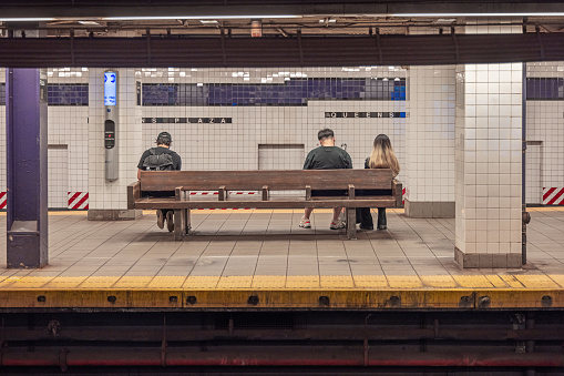 Long Island City, Queens, New York, NY, USA - July 9th 2022: Three adult people sitting on a bench at the Queens Plaza underground subway station