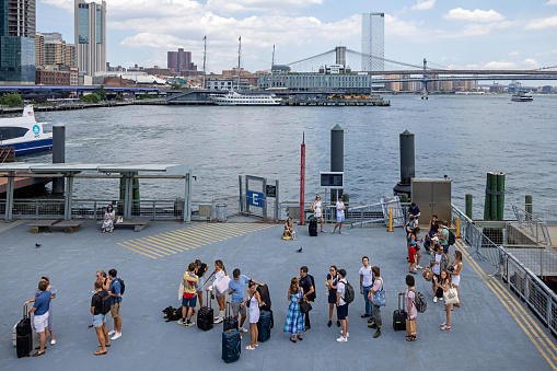 Manhattan, New York, NY, USA - July 9th 2022: People standing on the Pier 11 / Wall Street and waiting for one of the ferries taking commuters round Manhattan and cross the rivers
