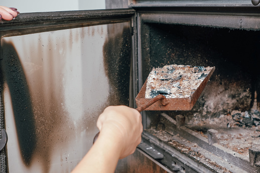 Fireplace cleaning. A woman's hand holds a shovel with ash in a burnt-out fireplace.