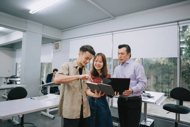 Asian Chinese adult student showing Malay lecturer on his note pad homework in classroom stock photo