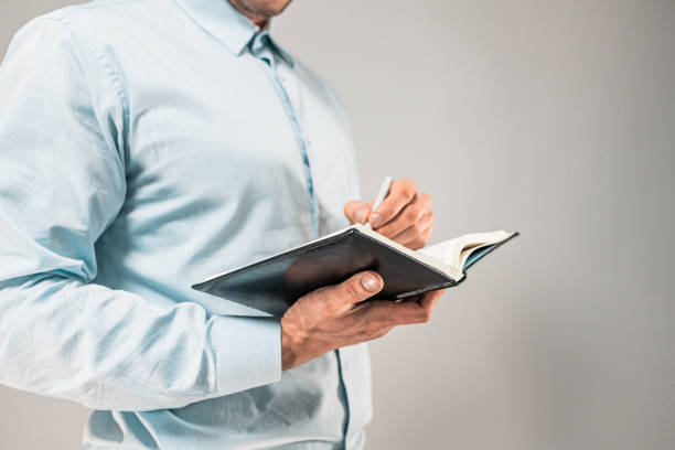 istock a man in a shirt holding a notebook in his hand and taking notes in it with a pen. 1418776300
