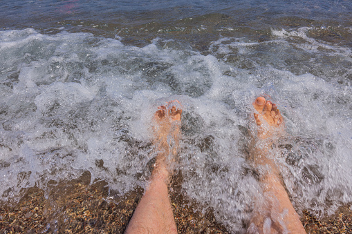 Close up view of feet through rolling waves. Summer tourism concept. Greece.