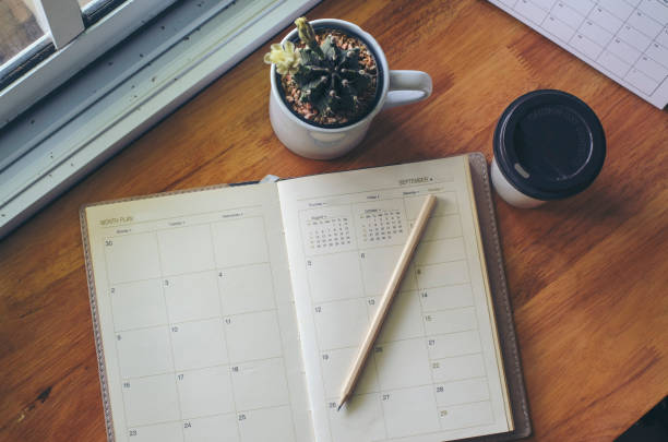 istock Diary, Calendar, and agenda for Event Planner to plan timetable, appointment, organization, and management on office table. Desktop Calender and coffee placed on wooden desk. Calendar Background Concept 1418783678