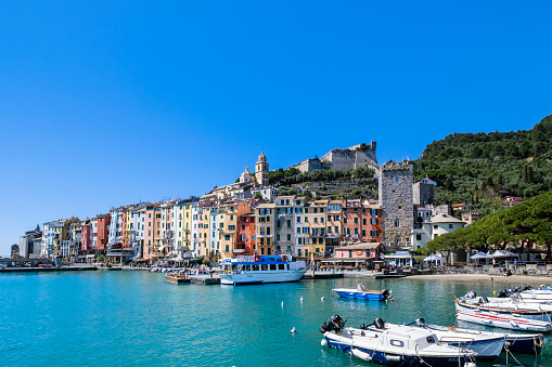 Pastel colored buildings lined up on the promenade of Porto Venere; in background, perched on the hill, are the castle and the church