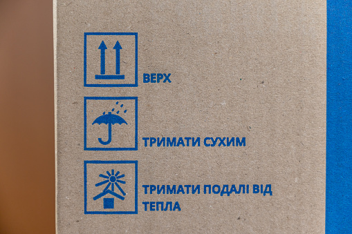 Markings on the cardboard box. Three blue shipping symbols. The inscriptions in Ukrainian mean UP, HOLD DRY, HOLD FAR FROM HEAT. Selective focus.