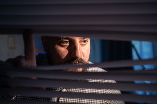 Indian man looking through window blind with facial expressions. Agoraphobia concept