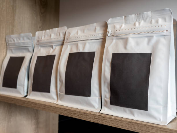 primer plano vacío etiqueta negra en blanco, papel artesanal de embalaje moderno de bolsa de café blanco. etiqueta adhesiva de plantilla de maqueta. fila de papel con cremallera de embalaje de bolsa para grano de café que se muestra en un estante de mad - consumerism ground coffee packaging coffee fotografías e imágenes de stock