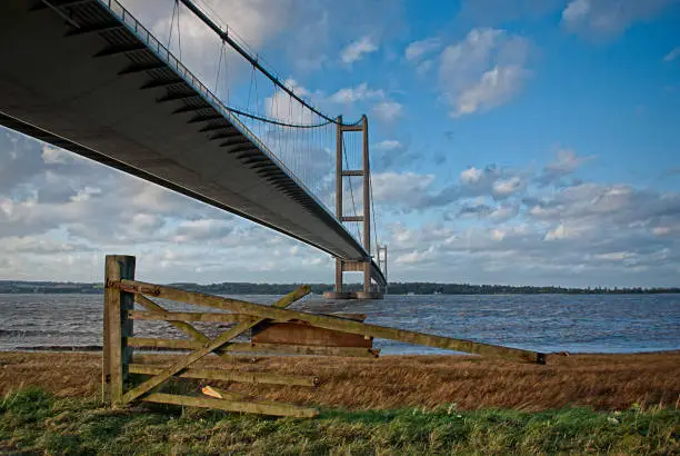 View from under the Humber Bridge looking from south to north, with broken gate in foreground, blue and cloudy sky