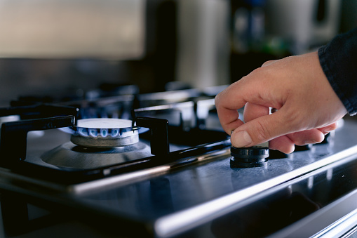 A hand turns on a stove fired by natural gas.