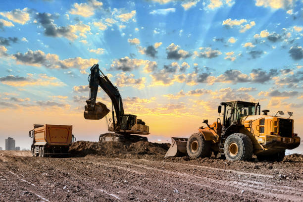 excavadoras trabajando en el sitio de construcción al atardecer - earth mover digging land bulldozer fotografías e imágenes de stock