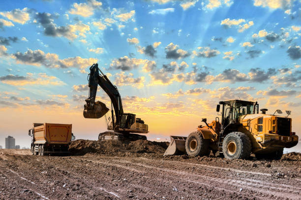 excavatrices travaillant sur un chantier au coucher du soleil - bulldozer photos et images de collection