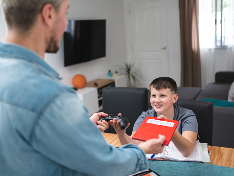 Caucasian boy swaps homework to his father and receives joystick for playing video games in exchange