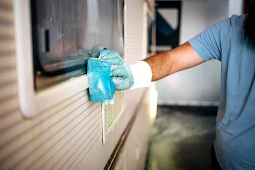 Man in work clothes wipes the glass of a camping trailer