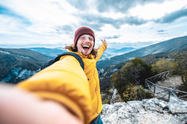 happy hiker taking selfie on the top of the mountain - young man having fun on weekend activity outside - travel blogger on social media live show - travel adventure winter cold imagens e fotografias de stock