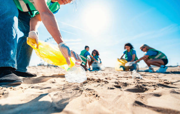 Group of eco volunteers picking up plastic trash on the beach - Activist people collecting garbage protecting the planet - Ocean pollution, environmental conservation and ecology concept stock photo