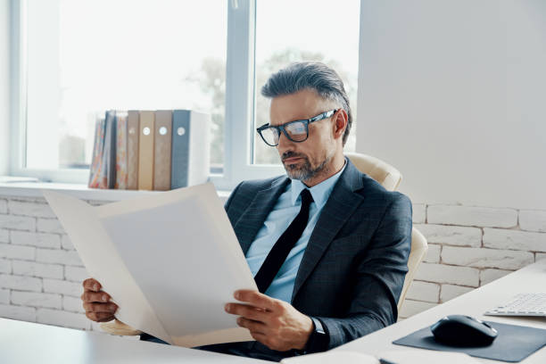 istock Confident mature man in formalwear doing some paperwork while sitting in the office 1418806711