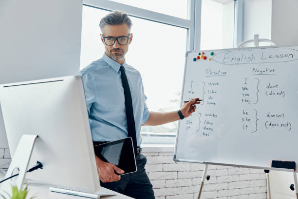 istock Confident English teacher pointing whiteboard while having web conference at the classroom 1418807626