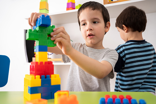 Little boy playing with colourful educational toy blocks on the table at preschool or kindergarten. Kid having fun while engaged in creative learning and development