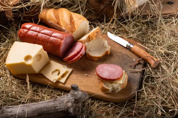 Photo of Slicing sandwiches from sausage and hard cheese. Fresh baguette and sausage.