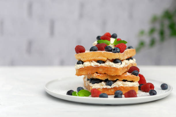 Dessert for breakfast. Fresh Viennese or Belgian waffles on a plate with fresh raspberries and blueberries and whipped cream.