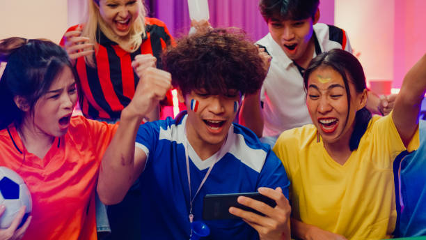 Group of happy Asia teen sit on couch watch cheer sport online soccer games world cup on cell phone at night. Group of happy Asia teen sit on couch watch cheer sport online soccer games world cup on cell phone at night. Shouting Get in wonderful goal excited scream, Football Winning facial expression concept. soccer bet online stock pictures, royalty-free photos & images