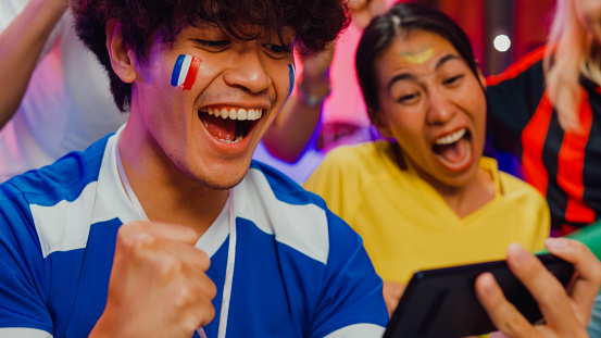 Close-up Group of happy Asian teen sit on couch watch cheer sport soccer games world cup championship together on smartphone at night. Shouting strike goal excited scream, facial expression concept.